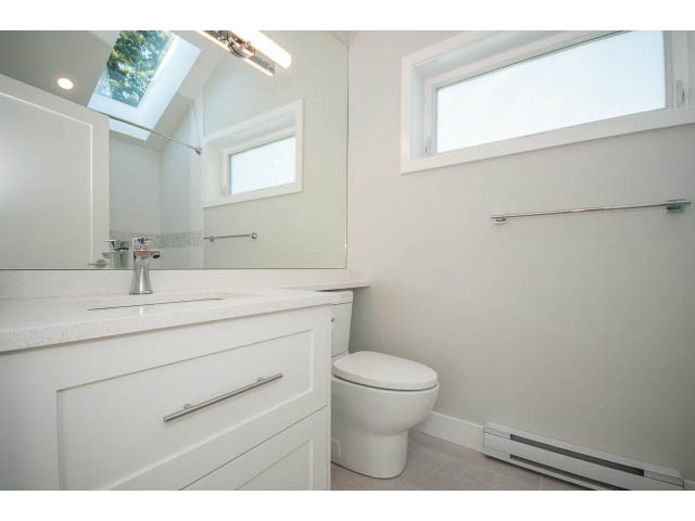 Bright bathroom with white vanity, toilet, and bathtub, natural light from skylight and window. - 4216 W 10th Ave, Vancouver West Side