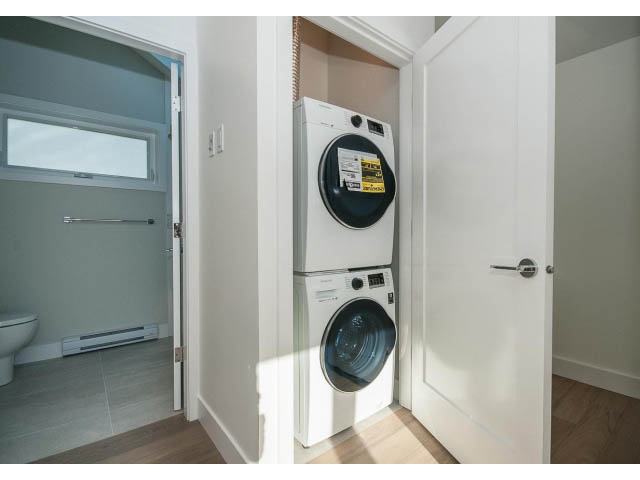 Bright laundry room with stacked washer and dryer, hardwood floors, and a partially open door leading to a bathroom.