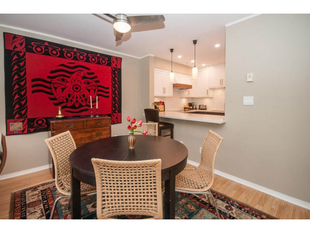 Furnished dining area with wicker chairs and a dark wooden table, hardwood floors, and a vibrant wall tapestry.