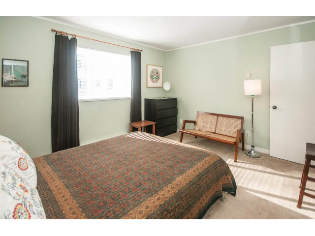 Bright bedroom with patterned bedspread, wooden chair, and window with curtains. - 301 - 2288 Laurel St, Vancouver West Side