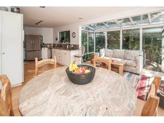 Furnished living room with granite countertops and hardwood floors, leading to a sunroom with large windows. - 3855 Bayridge Ave, West Vancouver