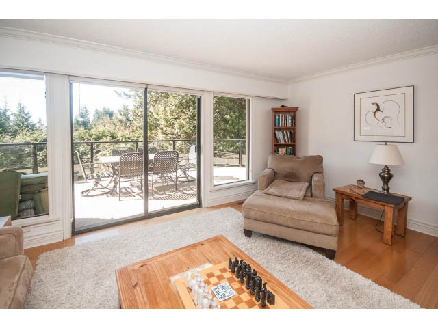 Spacious living room with hardwood floors, large windows, and a chess set on a wooden table. - 3855 Bayridge Ave, West Vancouver