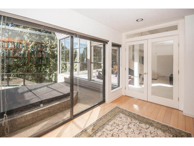 Bright sunroom with hardwood floors and city view, featuring a large sliding glass door and a cozy corner bench. - 3855 Bayridge Ave, West Vancouver