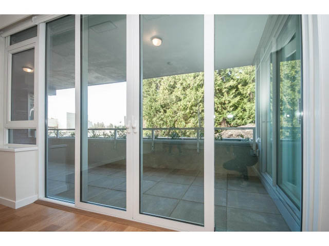 Bright living room with large glass doors leading to a patio, hardwood floors, and a city view. - 204 - 788 Arthur Erickson Pl, West Vancouver