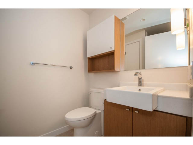 Bright bathroom with white sink, wooden cabinets, and a toilet. - 204 - 788 Arthur Erickson Pl, West Vancouver