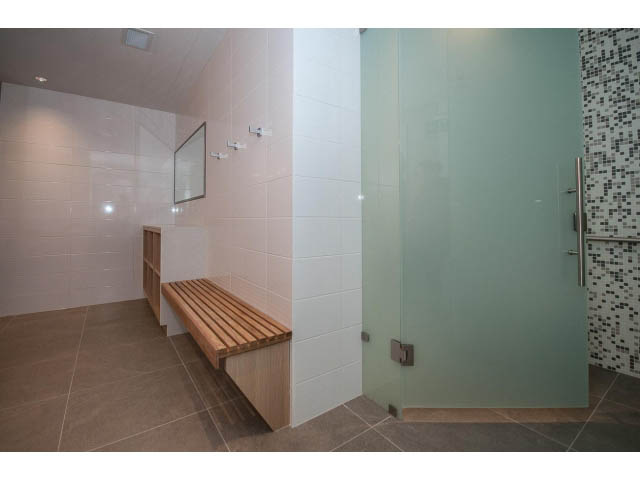 Furnished bathroom with glass shower, wooden bench, and modern tile. - 204 - 788 Arthur Erickson Pl, West Vancouver