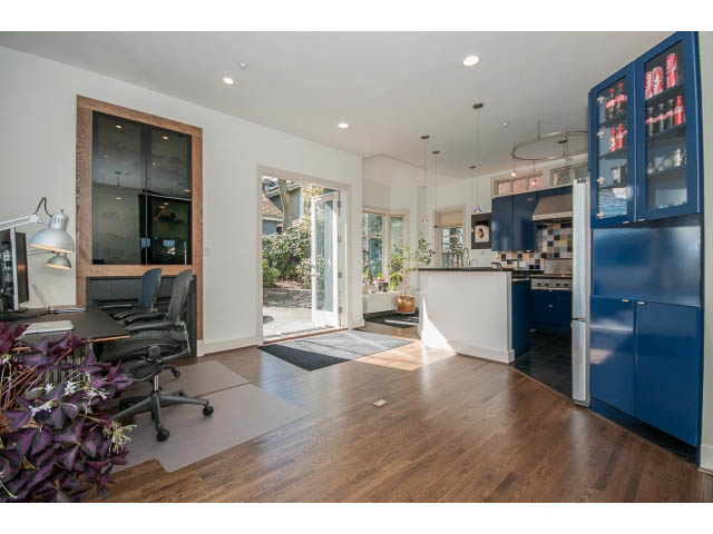 Bright kitchen with blue cabinets and hardwood floors, open to a cozy office area. - 3131 Collingwood St, Vancouver West Side