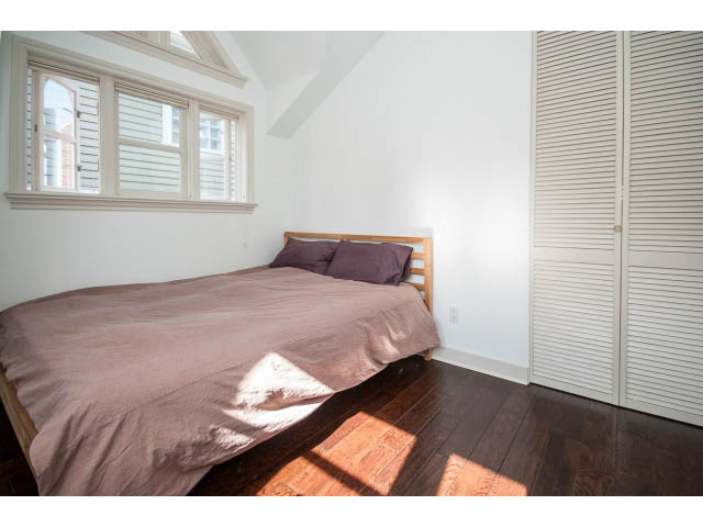 Bright bedroom with wooden floors and large windows, featuring a neatly made bed with a brown duvet. - 3131 Collingwood St, Vancouver West Side
