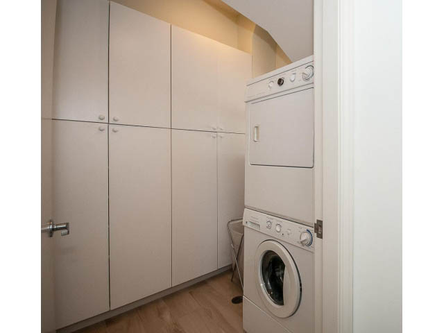 Laundry room with stacked washer and dryer, white cabinets, hardwood floors. - 3131 Collingwood St, Vancouver West Side
