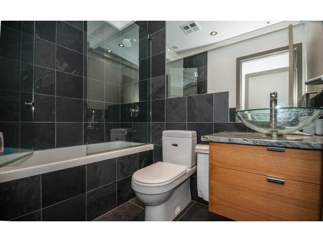 Modern bathroom with dark tiles, glass shower, and wooden vanity. - 2404 - 1500 Hornby St, Vancouver Downtown