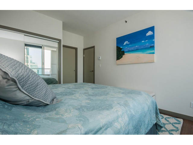 Furnished bedroom with blue patterned bedding and beach painting on wall. - 2404 - 1500 Hornby St, Vancouver Downtown