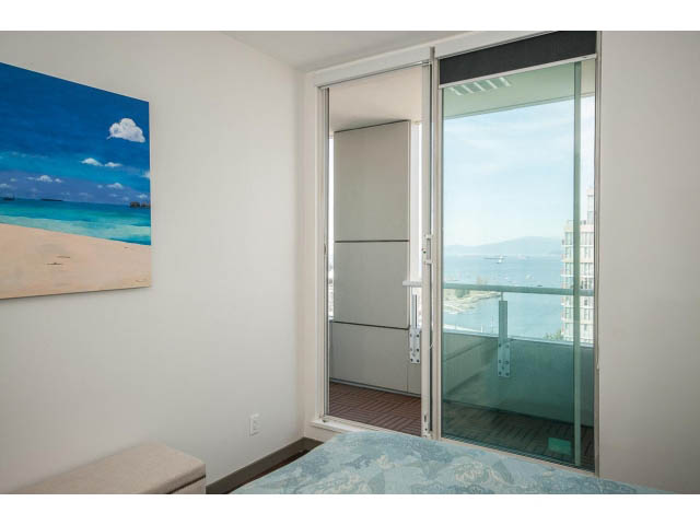 Furnished bedroom with a beach-themed painting and a sliding glass door leading to a balcony with a city view.