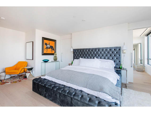 Bright, modern penthouse bedroom with tufted headboard, hardwood floors, and a vibrant orange chair. - 1901 - 1171 Jervis St, Vancouver Downtown