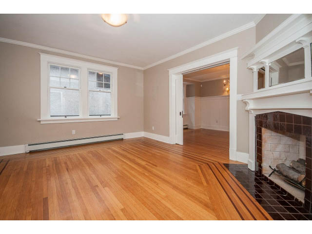 Bright living room with hardwood floors and a fireplace, leading to a kitchen area. - 769 West 20th Ave, Vancouver West Side