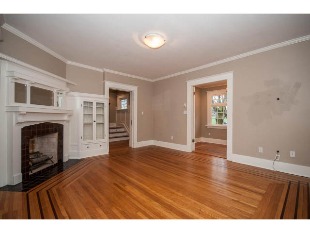 Bright living room with hardwood floors and a fireplace, leading to a kitchen area. - 769 West 20th Ave, Vancouver West Side