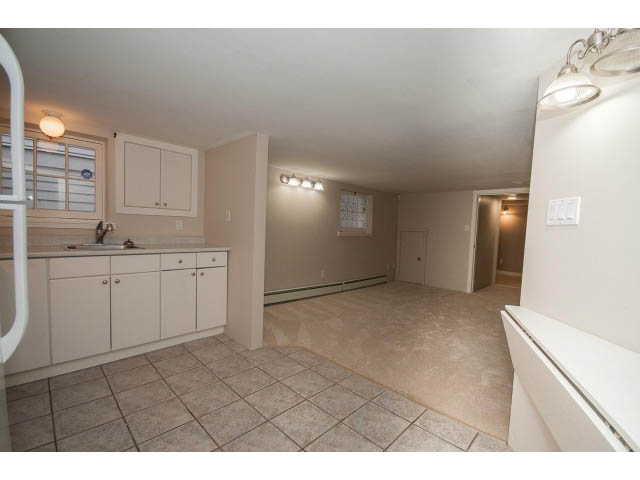 Bright kitchen with white cabinets and tiled floors, leading to a living area. - 769 West 20th Ave, Vancouver West Side