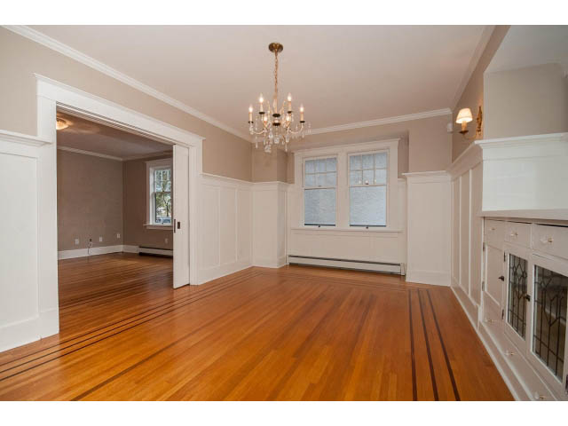 Bright living room with hardwood floors and a chandelier, leading to a kitchen with white cabinetry. - 769 West 20th Ave, Vancouver West Side