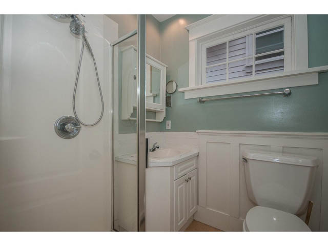 Bright bathroom with white cabinetry, shower, and window with shutters. - 769 West 20th Ave, Vancouver West Side