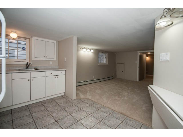 Bright kitchen with white cabinets and tiled countertops, leading to a spacious living area with tiled flooring.