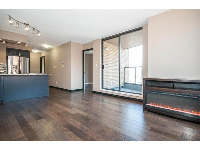 Bright living room with hardwood floors and modern fireplace, open to kitchen with stainless steel appliances.