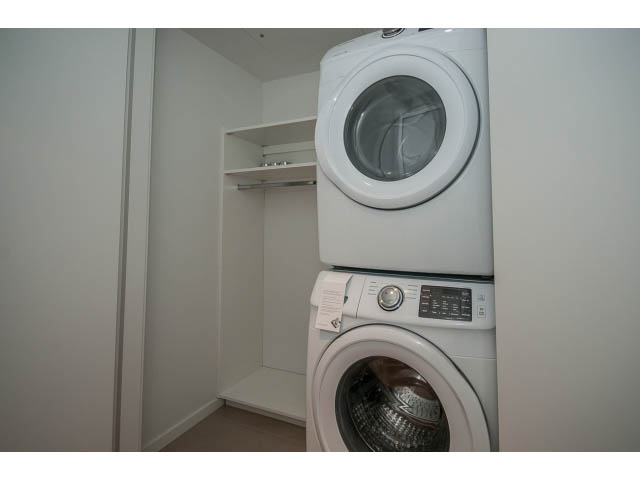 Laundry room with stacked washer and dryer, white shelves above. - 804 - 1171 Jervis St, Vancouver Downtown