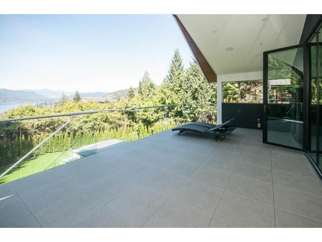 Spacious outdoor patio with glass railings, overlooking lush greenery and distant mountains. - 5235 Headland Dr., West Vancouver