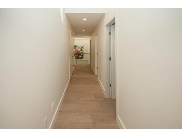 Bright hallway with hardwood floors and a modern painting at the end. - 5235 Headland Dr., West Vancouver