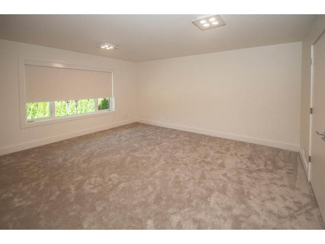 Bright bedroom with beige carpet and white walls, featuring a window with a view of greenery. - 5235 Headland Dr., West Vancouver