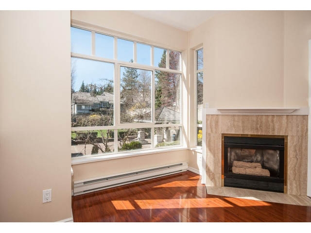 Bright living room with large windows, hardwood floors, and a fireplace. - 204 - 630 Roche Point Drive, North Vancouver