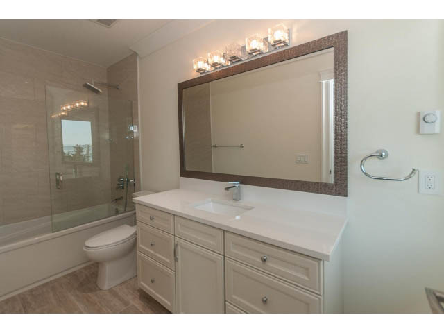 Bright bathroom with white cabinetry, marble countertops, and a large mirror. - 2333 Mathers Ave, West Vancouver
