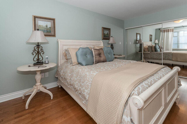 Spacious master bedroom with light blue walls, hardwood floors, and a large sleigh bed with patterned bedding.