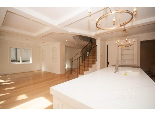 Bright kitchen with white marble countertops and hardwood floors, featuring a chandelier and a staircase leading to the...