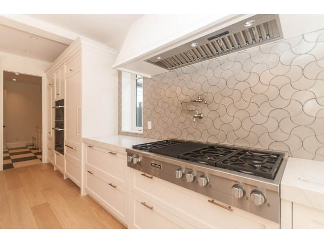 Bright kitchen with white cabinets, marble countertops, and a unique wave-patterned backsplash. - 6448 Argyle Ave, West Vancouver