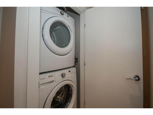 Bright laundry room with stacked washer and dryer, white cabinets. - 303 - 615 East 3rd Street, North Vancouver
