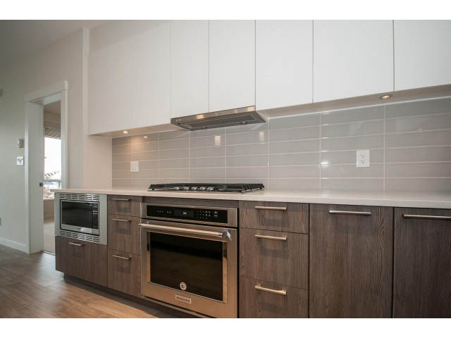 Bright kitchen with modern appliances, wooden cabinets, and a city view. - 303 - 615 East 3rd Street, North Vancouver