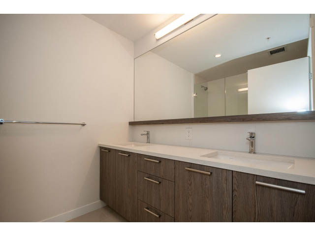 Furnished bathroom with modern sink, wooden cabinets, and large mirror. - 303 - 615 East 3rd Street, North Vancouver