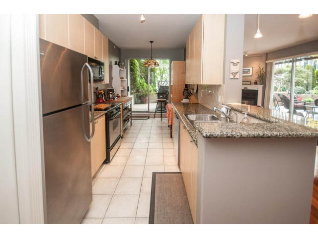 Bright kitchen with granite countertops and hardwood floors, leading to a cozy living area with a city view. - 310 - 160 E 13th St, North Vancouver