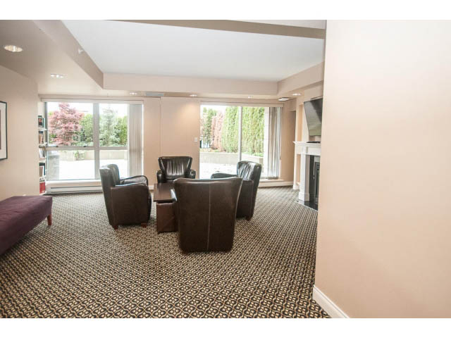 Furnished living room with patterned carpet, large windows, and a fireplace. - 310 - 160 E 13th St, North Vancouver