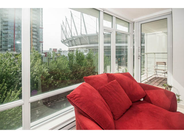 Furnished living room with red couch and city view through large windows. - 501 - 161 West Georgia St, Vancouver Downtown