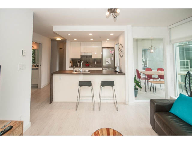 Bright kitchen with white cabinets and hardwood floors, open to a cozy living area. - 501 - 161 West Georgia St, Vancouver Downtown