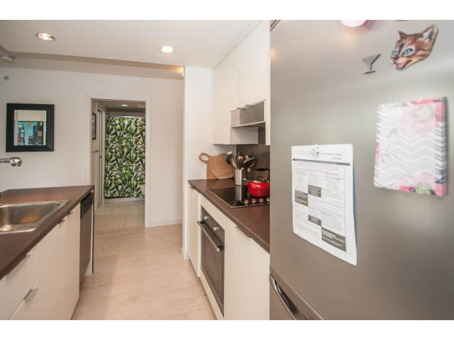 Bright kitchen with stainless steel appliances, white cabinets, and a red chair at the counter. - 501 - 161 West Georgia St, Vancouver Downtown