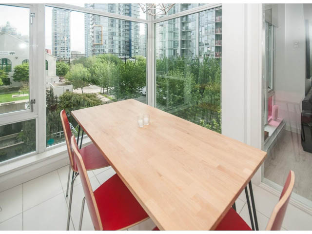 Bright dining area with wooden table, red chairs, and city view through large windows. - 501 - 161 West Georgia St, Vancouver Downtown