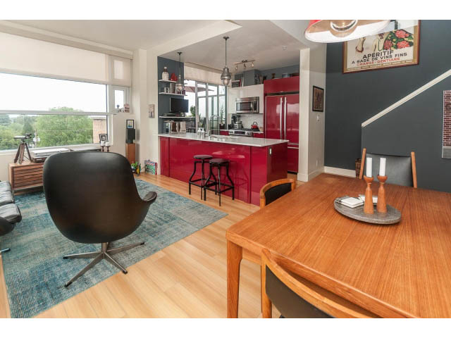 Bright kitchen with red appliances and hardwood floors, open to a cozy living area with a black chair and city view.
