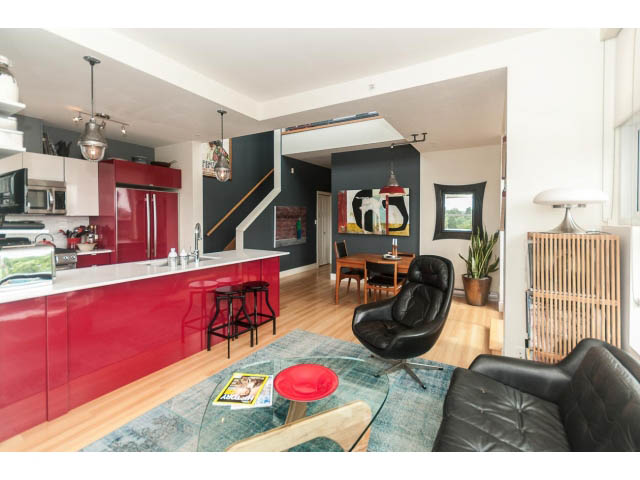 Bright kitchen with red cabinets and open-concept living area featuring black leather furniture and a glass coffee table.