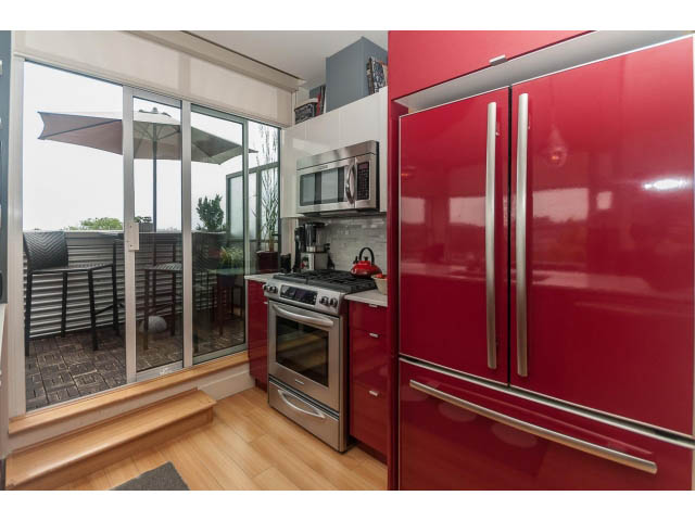 Bright kitchen with red cabinets, stainless steel appliances, and hardwood floors. - 4123 - 2250 Commercial Dr, Vancouver East Side