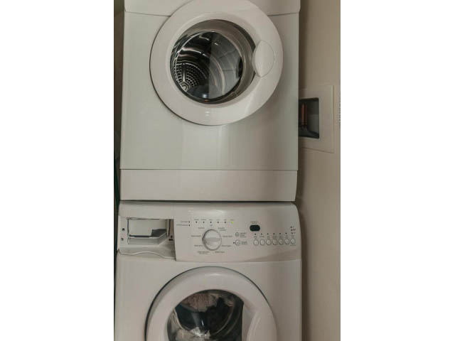 Bright laundry room with stacked washer and dryer, clean white surfaces. - 4123 - 2250 Commercial Dr, Vancouver East Side