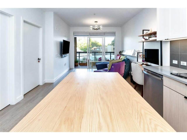 Bright kitchen with wooden countertops and hardwood floors, leading to a cozy living area with a city view.