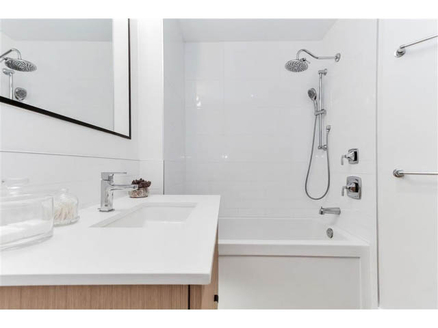 Bright bathroom with modern white fixtures and a large mirror. - 305 - 3205 Mountain Highway, North Vancouver