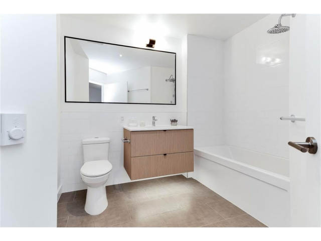 Furnished bathroom with modern sink, large mirror, and shower. - 305 - 3205 Mountain Highway, North Vancouver