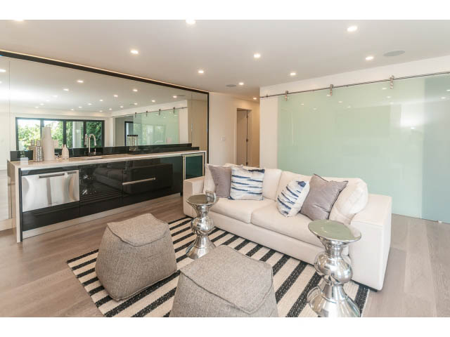Bright living room with modern furnishings, hardwood floors, and a glass wall leading to a kitchen. - 460 Hillcrest Street, West Vancouver